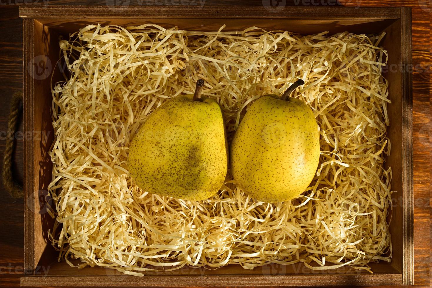 två mogna päron i en låda med spån på ett träbord, närbild, ovanifrån foto