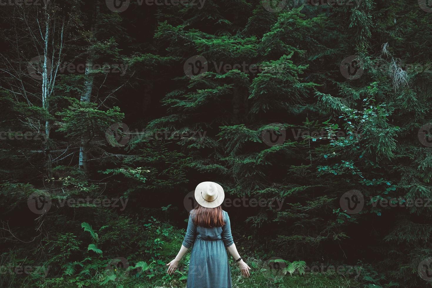 kvinna i en stråhatt och klänning står på en bakgrund av grön skog och träd foto