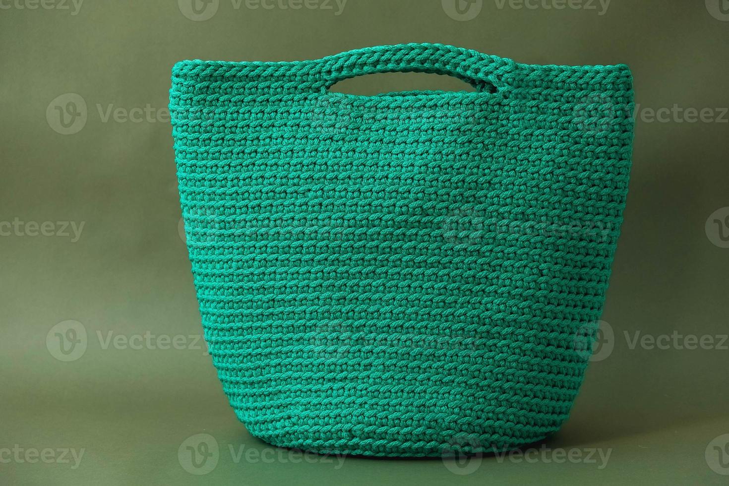 snygg kvinnas stickade gröna väska på grön bakgrund. kopiera, tomt utrymme för text foto