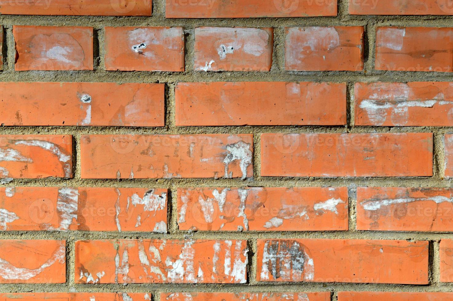 gammal orange tegelvägg. målad sliten väggyta. vintage röd tegelvägg med tecken på gamla annonser på den. urban fotobakgrund för design. byggnadsfasad med skadad puts foto
