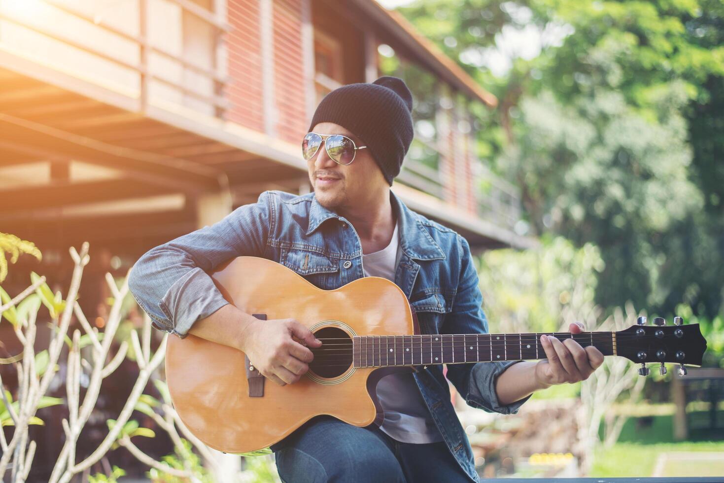 hipster man sitter medan du spelar gitarr och sjunger. foto