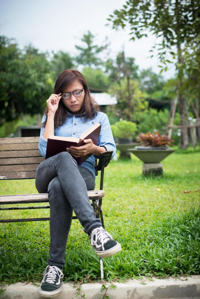 hipster charmig tjej koppla av i parken medan du läser bok, njut av naturen runt. foto