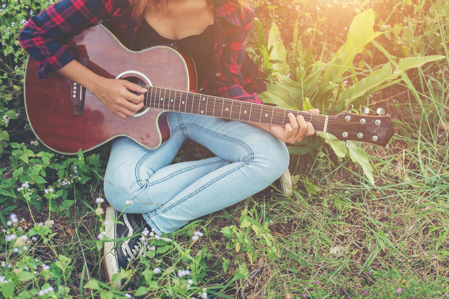 hipster kvinna händer spelar gitarr sitter på gräs i parken, koppla av med naturen. foto