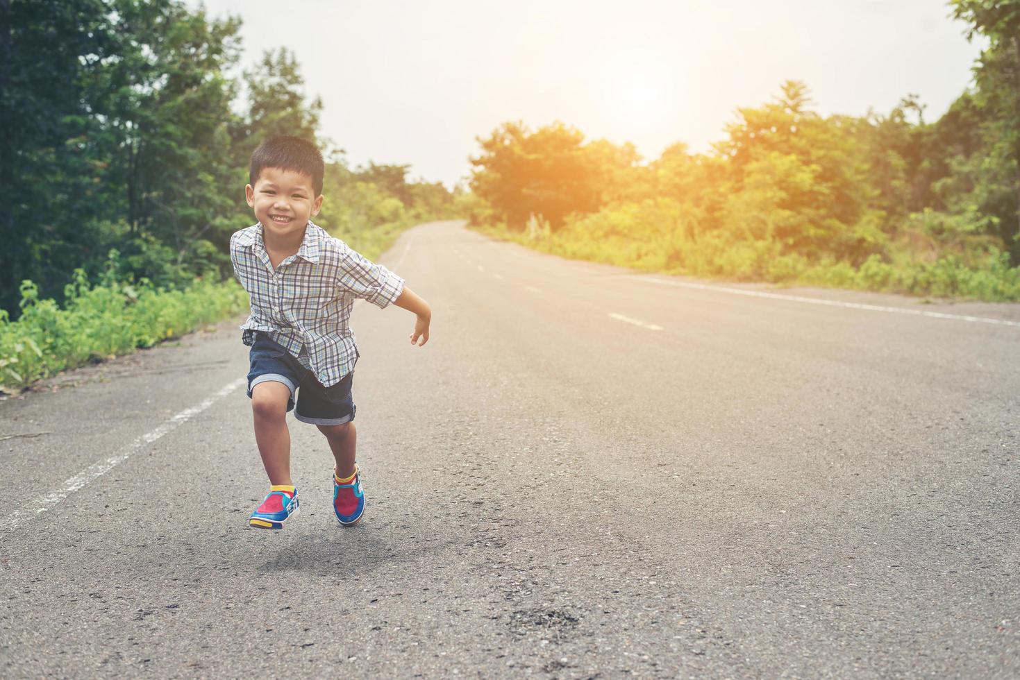 glad liten pojke i rörelse, smiley springer på gatan. foto
