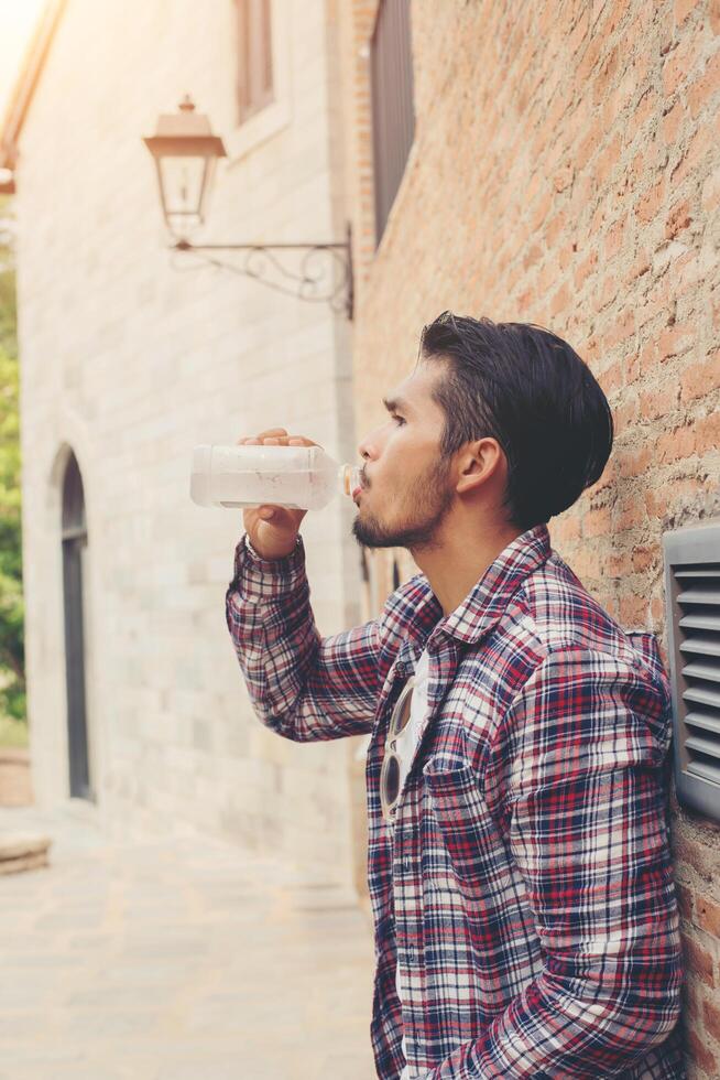 ung hipster skäggig man med vattenflaska i rutig skjorta framför urban bakgrund. foto