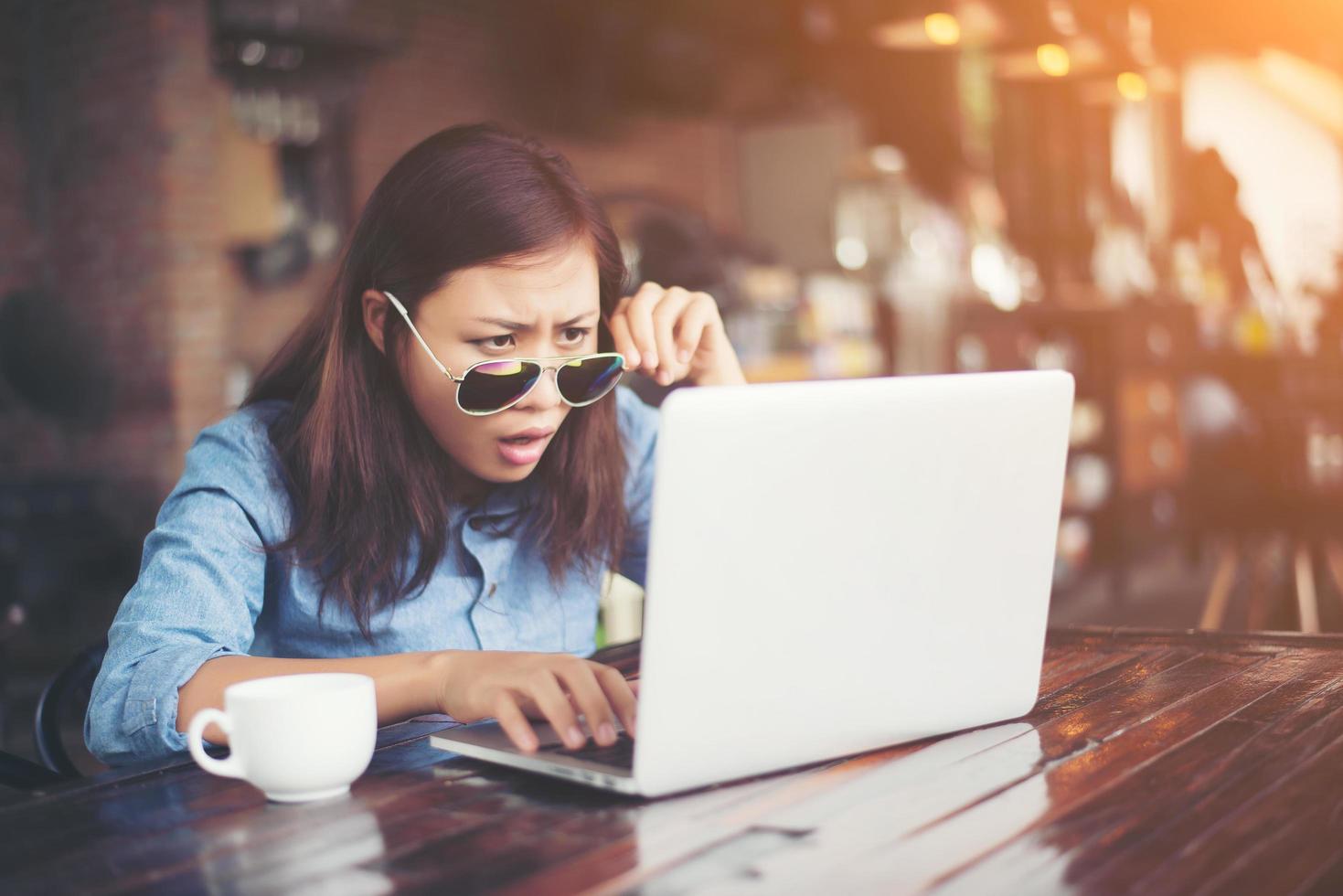 vacker ung hipsterkvinna som sitter på ett kafé, koppla av och lek med sin bärbara dator, hitta information om ledig tid, glad och rolig. livsstilskoncept. foto