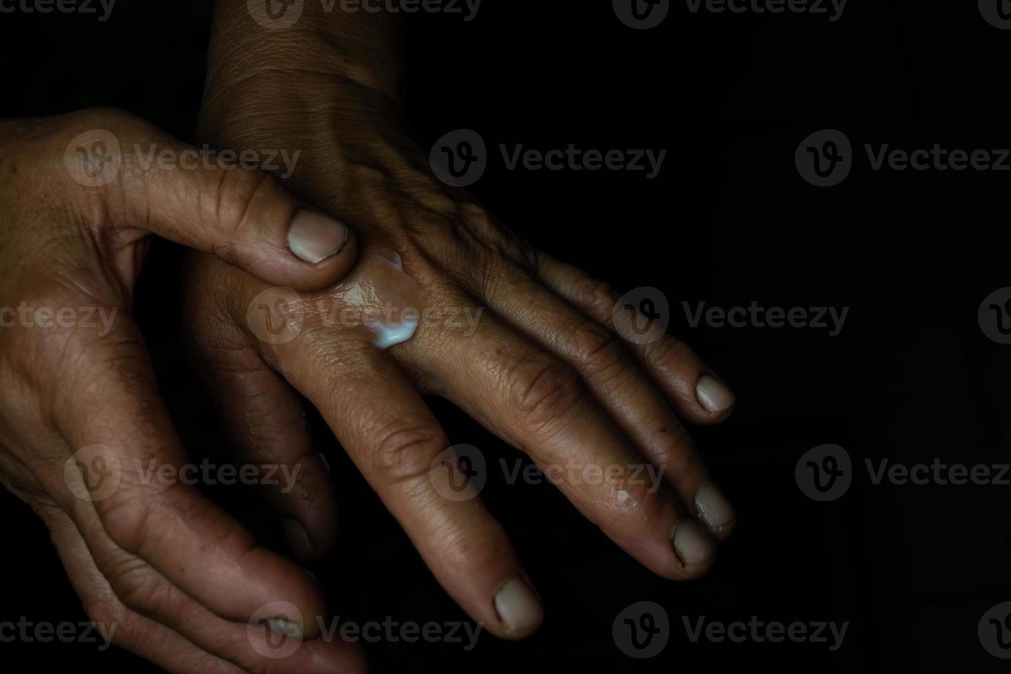 en äldre kvinna gnuggar in handkräm i skrynklig hud. foto
