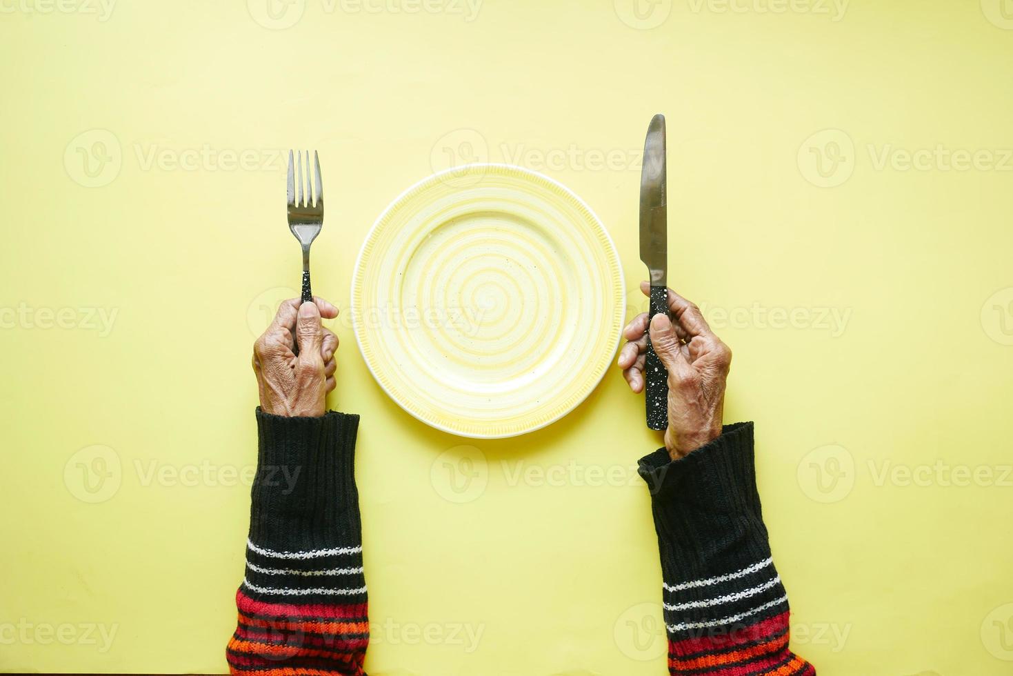 senior kvinnor håller bestick och tom tallrik på gul bakgrund foto