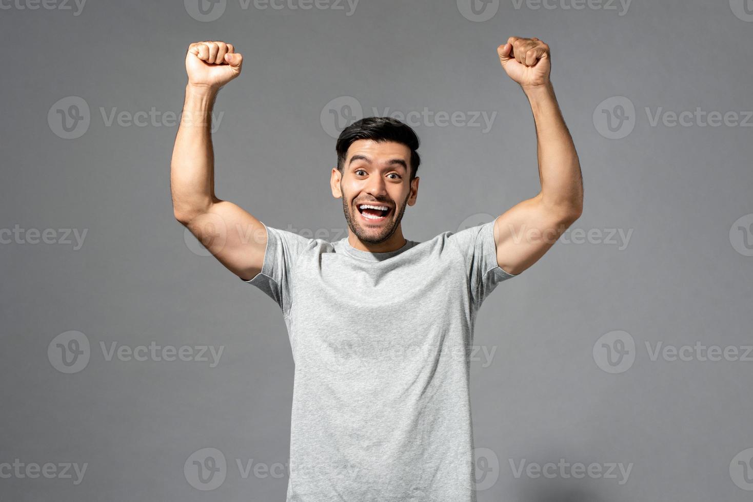 ung glad frisk kaukasisk man som ler och höjer nävarna på isolerad ljusgrå studiobakgrund foto