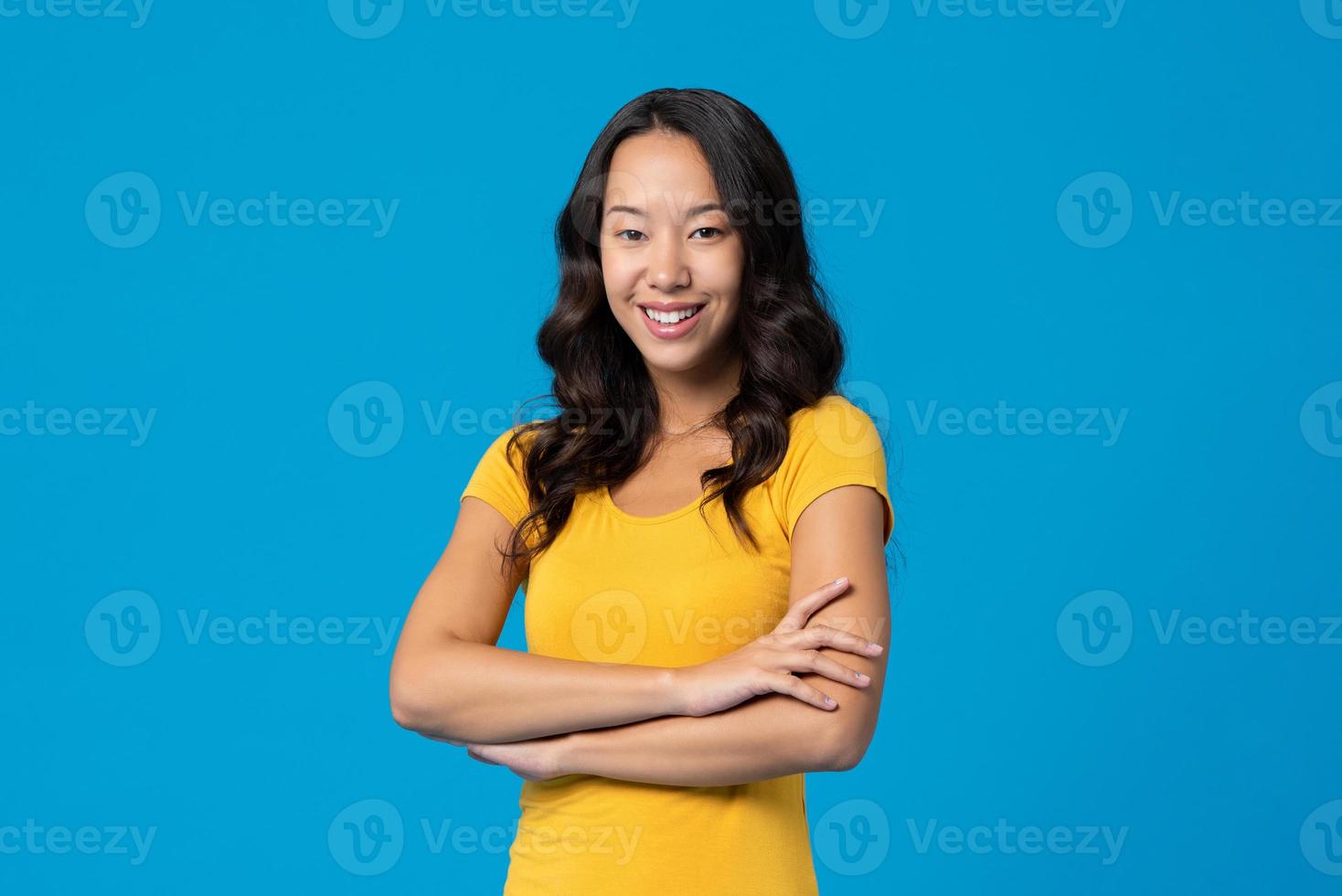 leende glad blandras ung millennial kvinna med armarna i kors isolerad på blå studio bakgrund foto