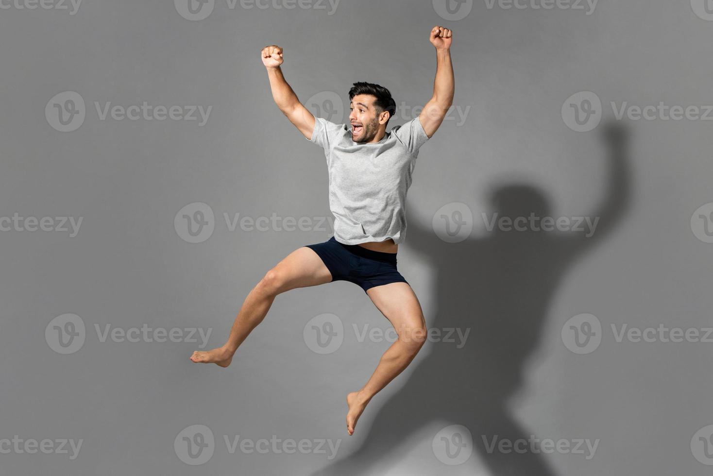 fullängdsporträtt av en ung frisk energisk man som bär nattkläder och hoppar i luften efter att ha vaknat från en god sömn på morgonen foto