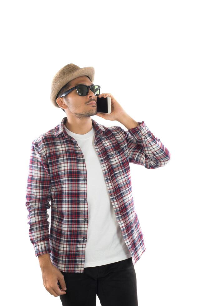 stilig hipster ung man i hatt och solglasögon står och pratar i mobiltelefon över vit bakgrund. foto