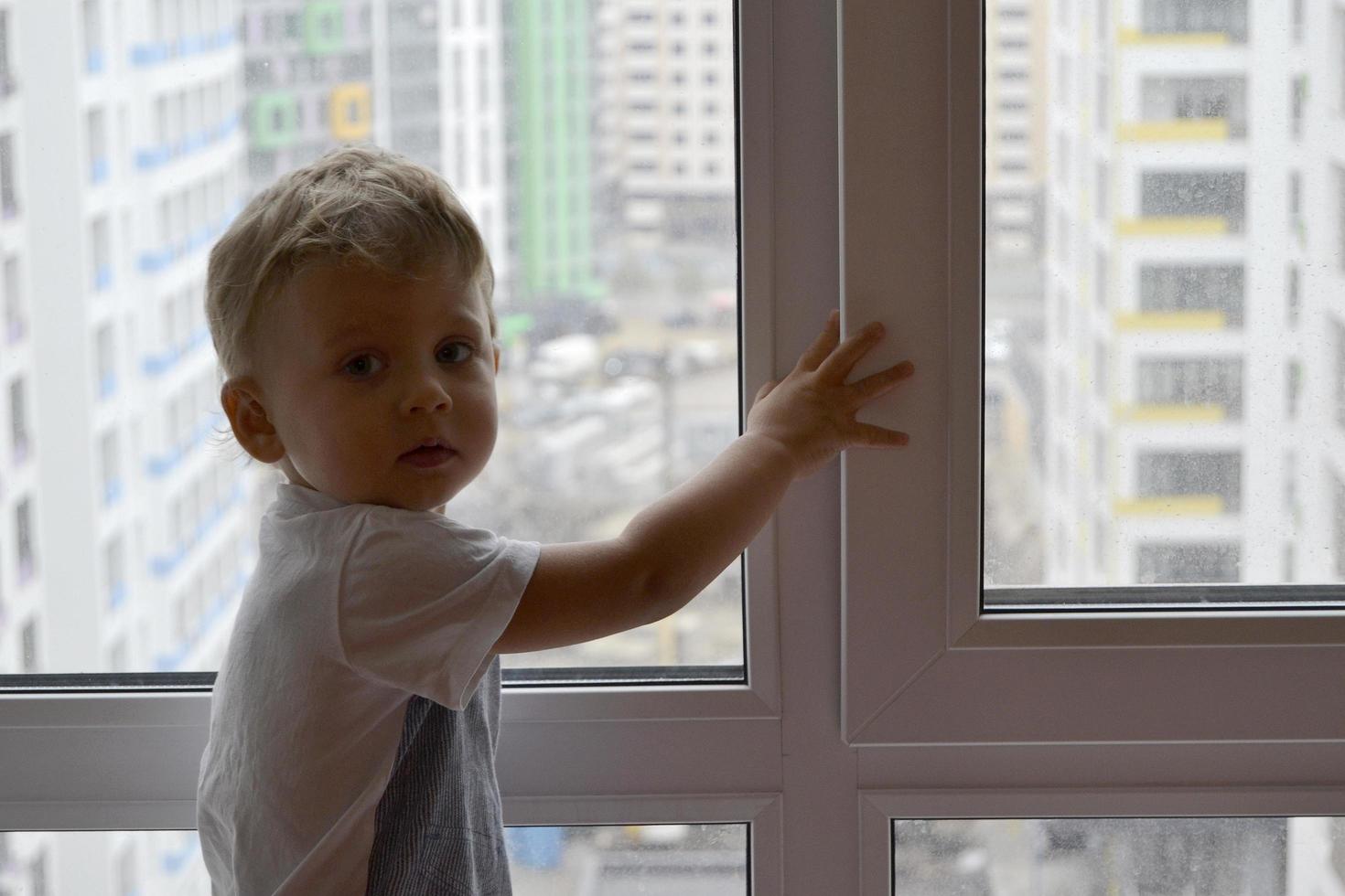 vacker baby pojke med barn ansikte poserar fotograf nära fönstret foto