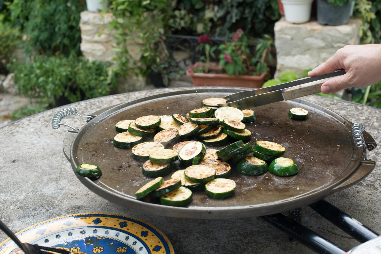 oigenkännlig person som förbereder skivad zucchini på en grill foto