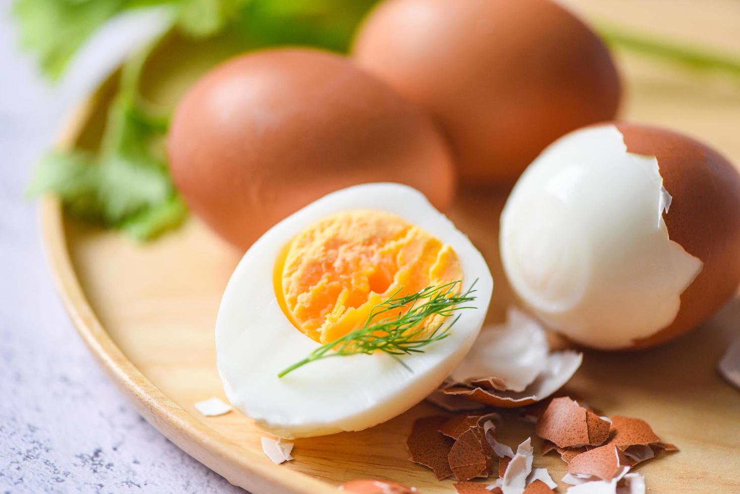ägg frukost, färska skalade ägg meny mat kokta ägg i en träplatta dekorerad med löv grön dill och äggskal, halverade äggulor för matlagning hälsosam mat foto