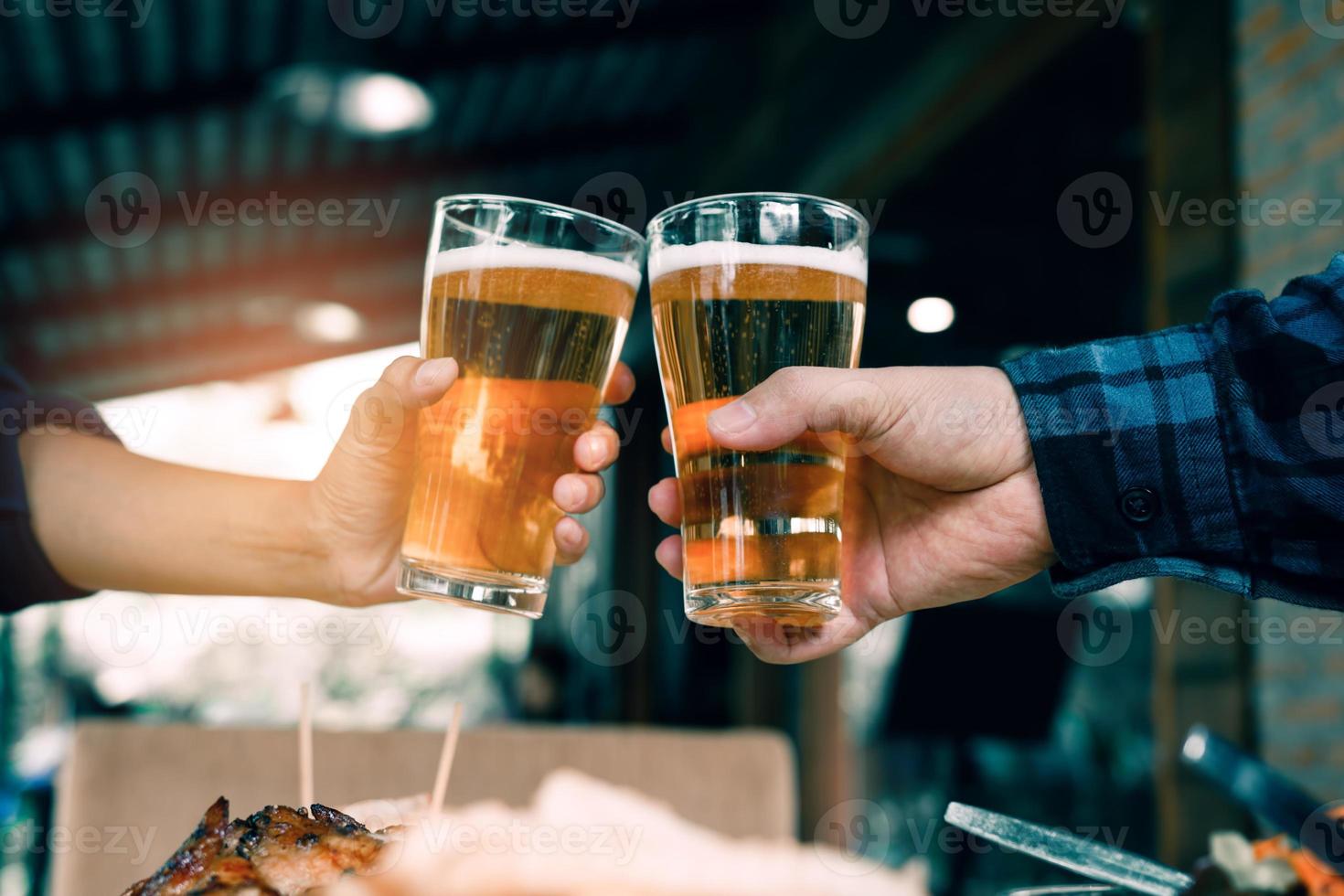 närbild på hand människor vänner skålar och klirrar med ett glas öl i restaurangen. foto