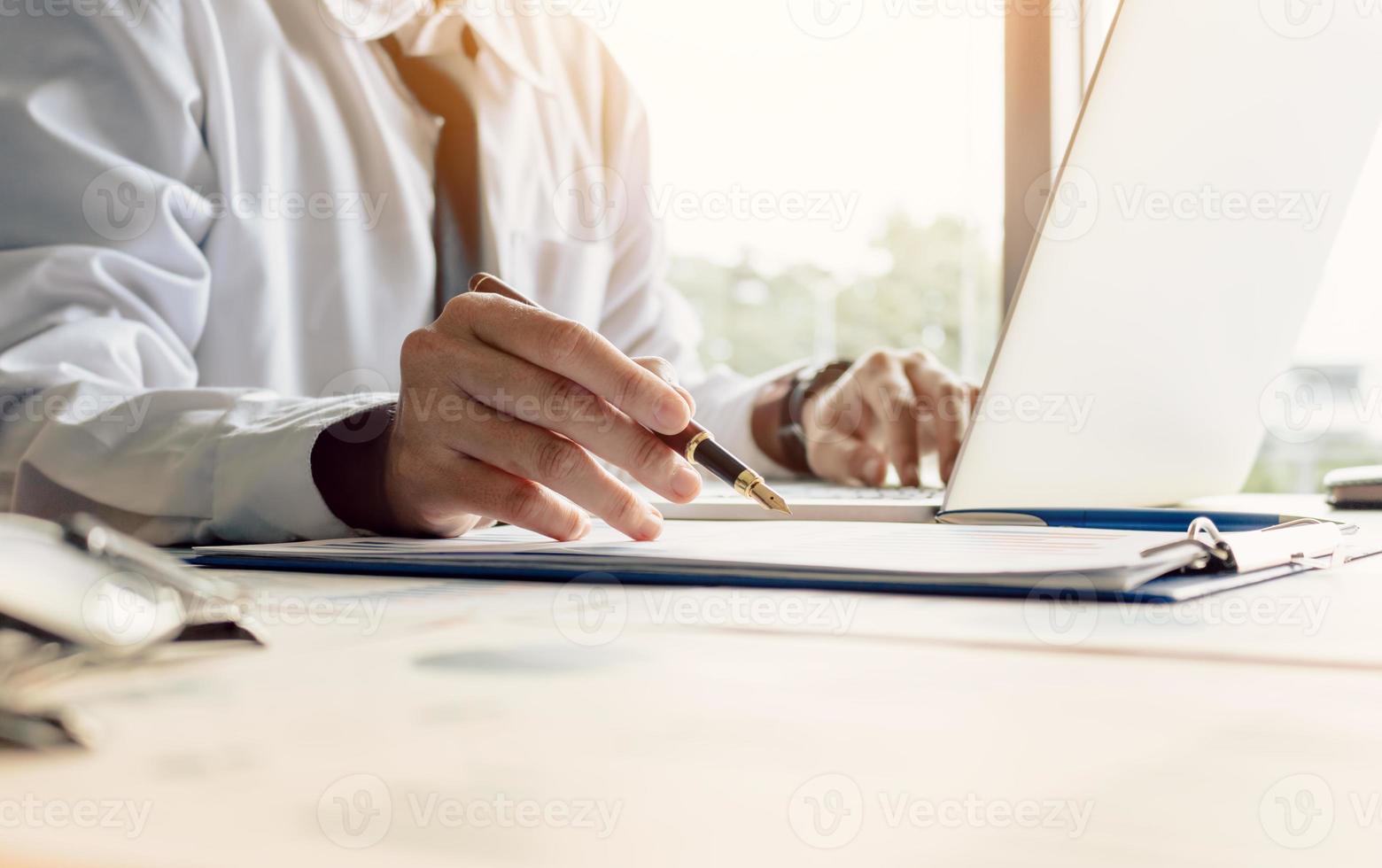affärsman sitter på kontor rum håller pennan pekar sammanfattande rapport graf och analysera med hjälp av bärbar dator för att söka informationsdata. foto