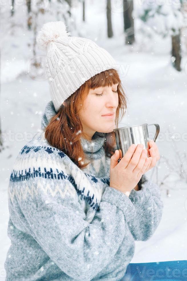 kvinna med en kopp te i händerna i en snötäckt skog foto