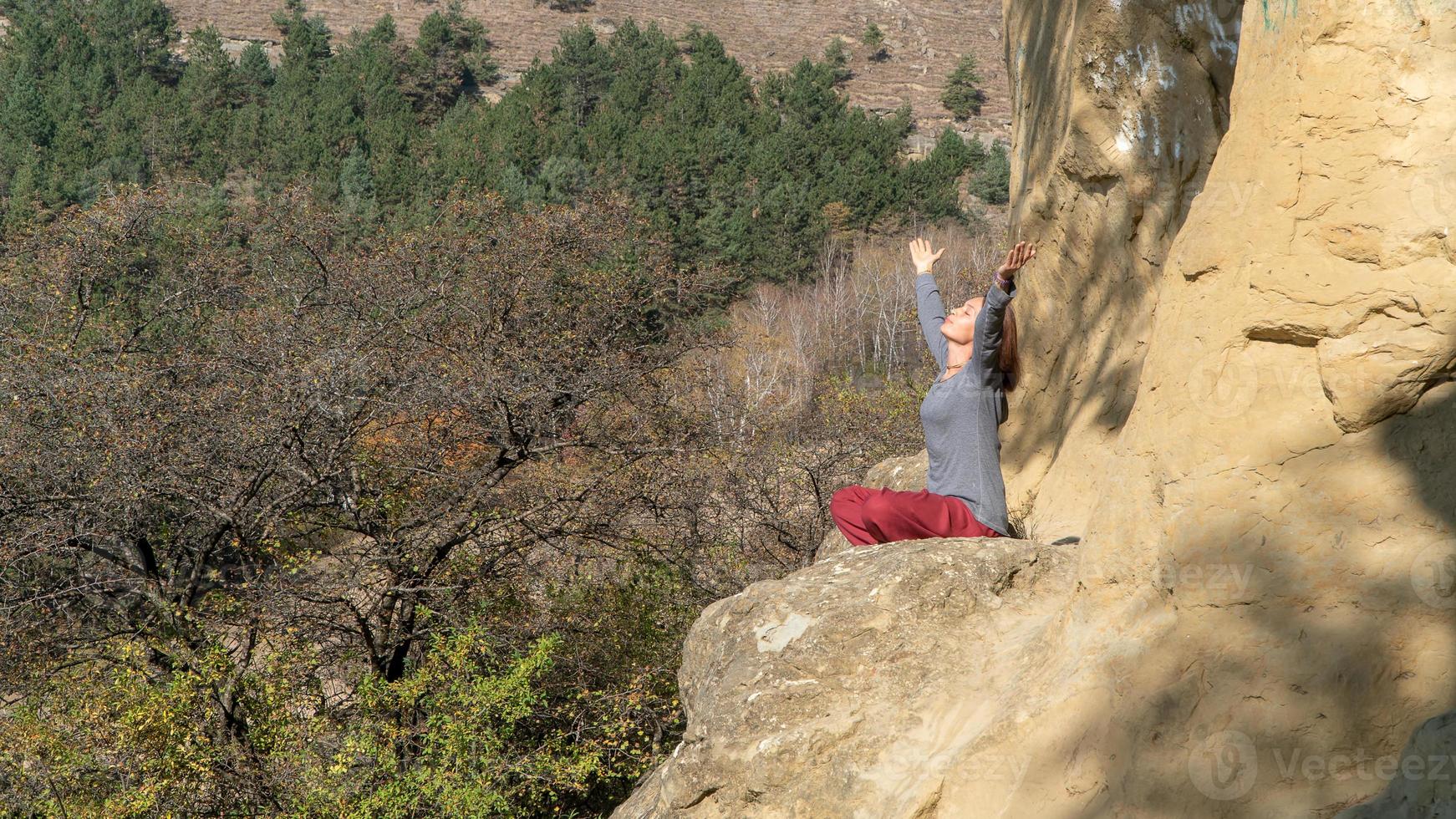 kvinna med slutna ögon och höjda armar sitter på ett berg i lotusställning i meditation en höstdag foto