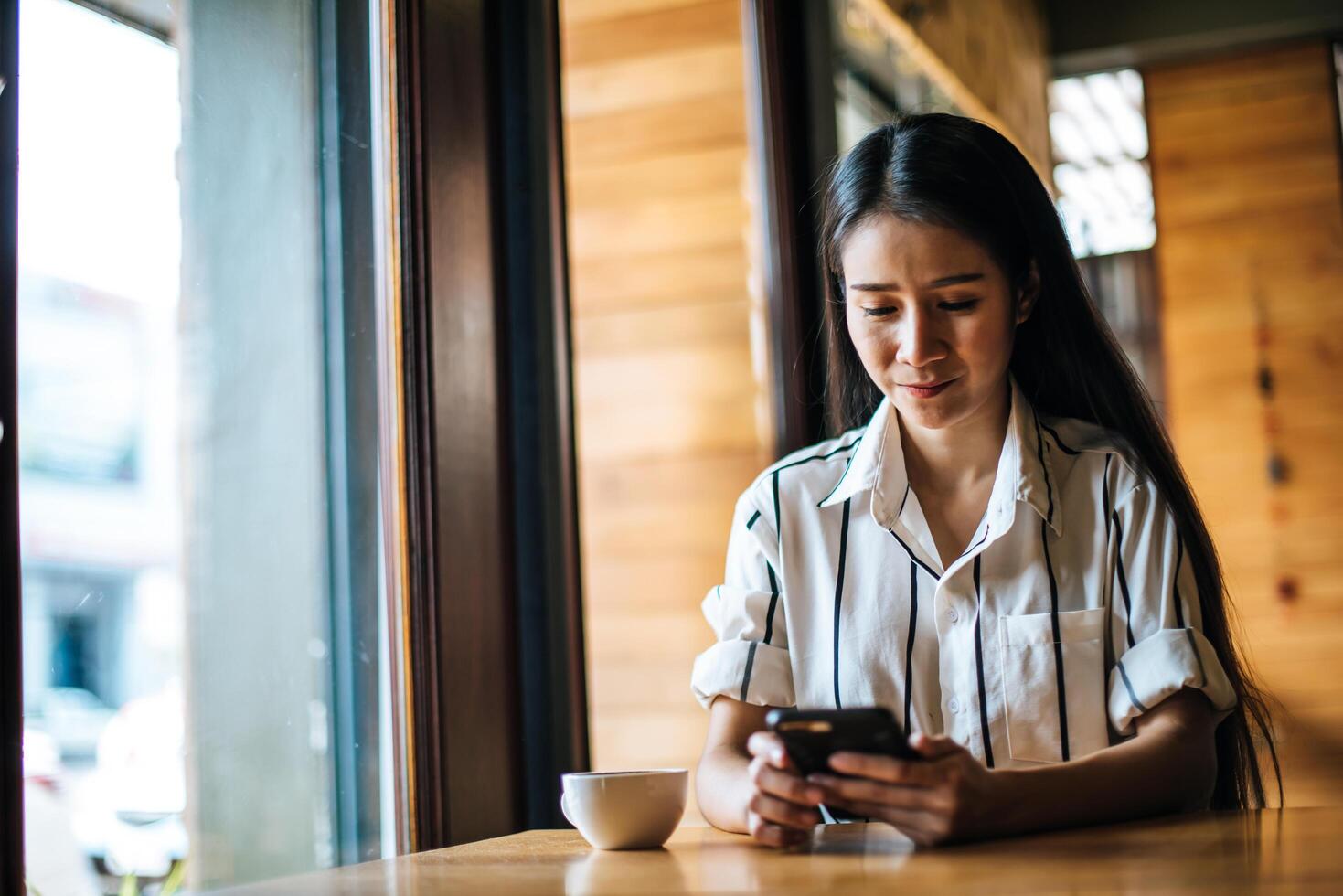 kvinna sitter och spelar sin smarta telefon på café foto