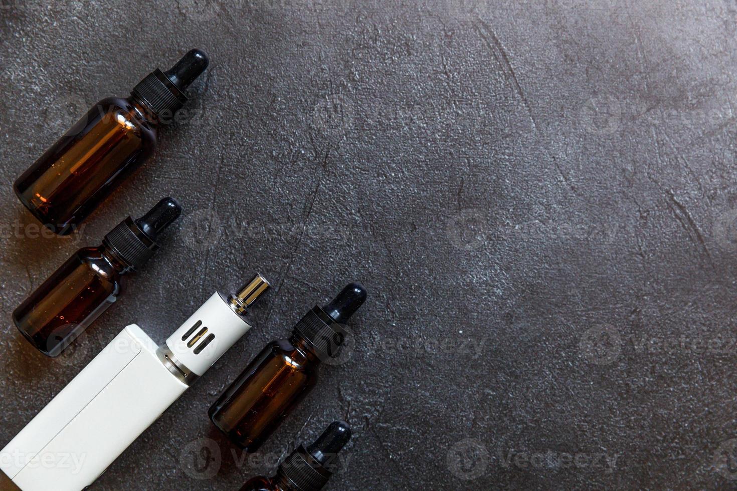 vaping enhet e-cigarett elektronisk cigarett och vätskeflaskor på mörk svart sten skiffer bakgrund. vapeapparat för alternativ rökning. vaping butik koncept. pryl för vaper. vaping tillbehör. foto