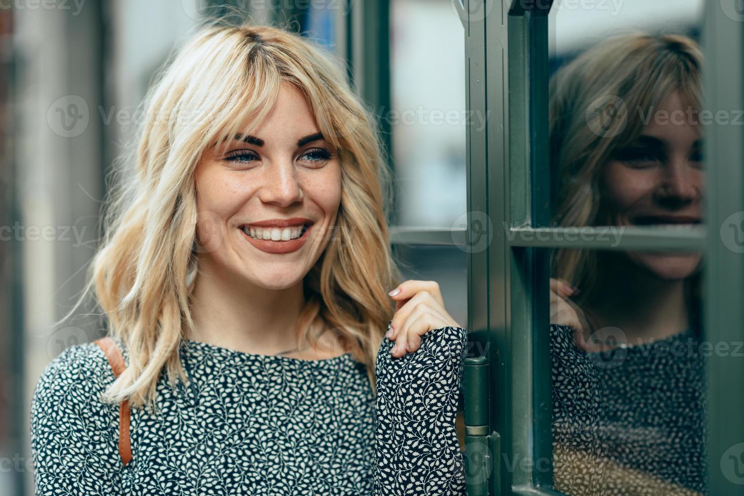 leende ung blond kvinna som står på urban bakgrund. foto