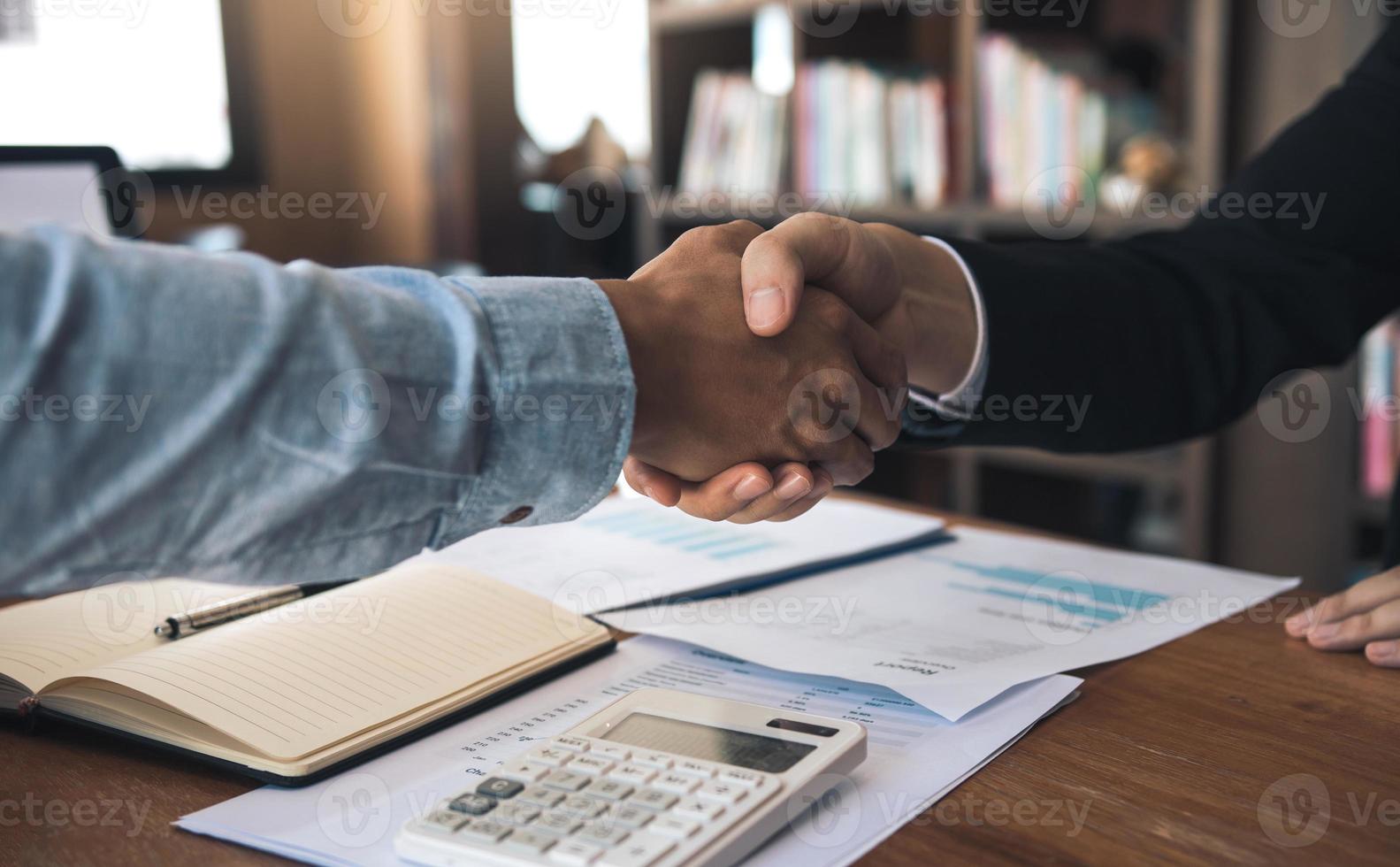 entreprenörers samarbetsavtal skakar hand i ett modernt kontor och finansiell pappersgraf på skrivbordet. foto