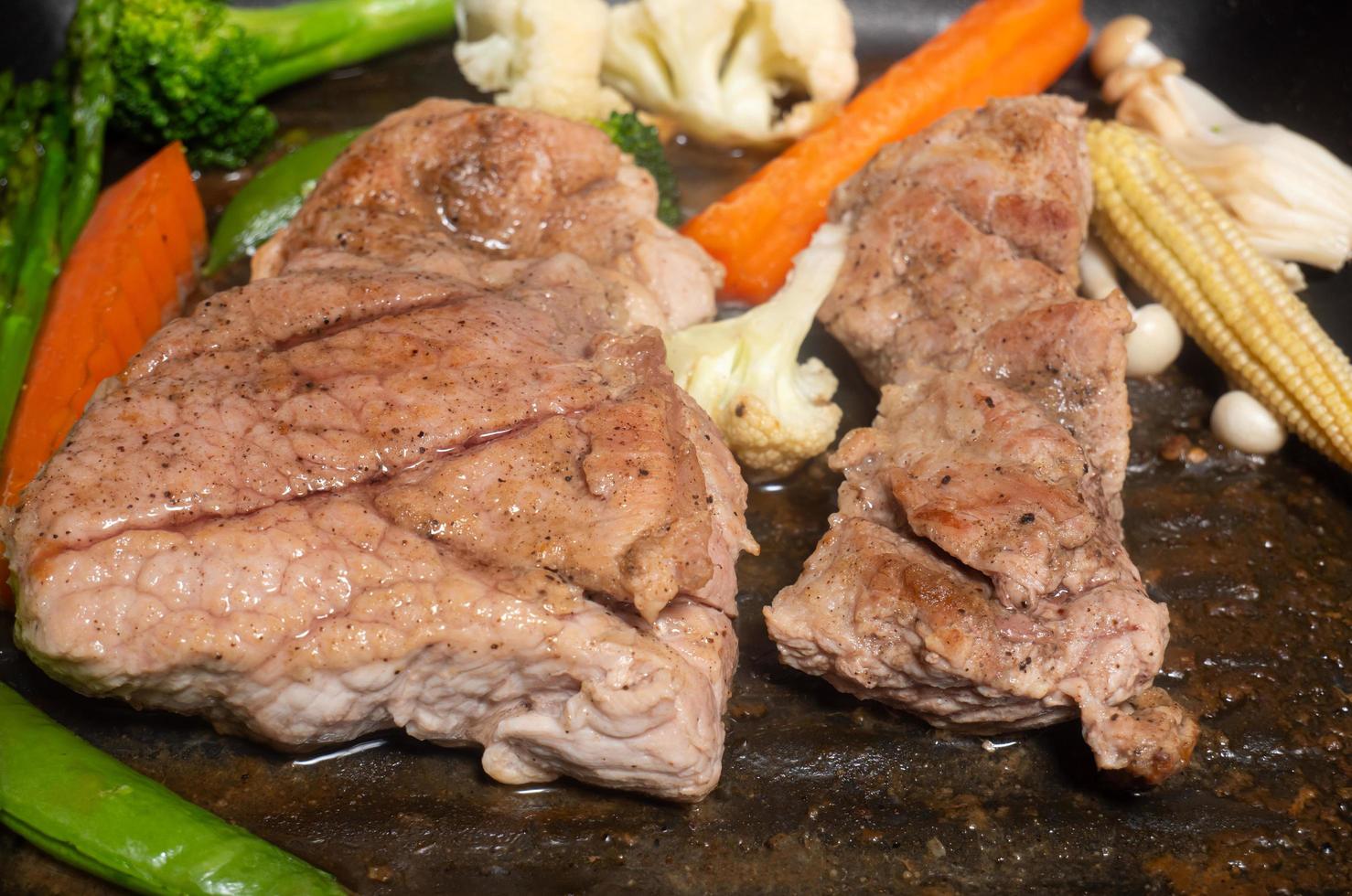 fläskbiff, svartpeppar, grillad på teflonpanna med grönsaker, sparris, broccoli, blomkål, morötter och svamp tillagade tillsammans med att baka kött i panna. foto