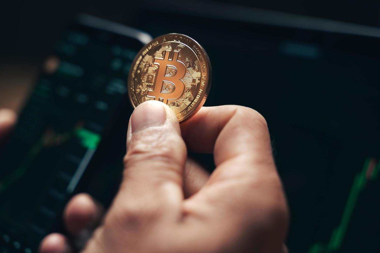 affärsman som håller gyllene bitcoin på datorhandel diagram skärm bakgrund. aktie, cryptocurrency trading koncept. foto