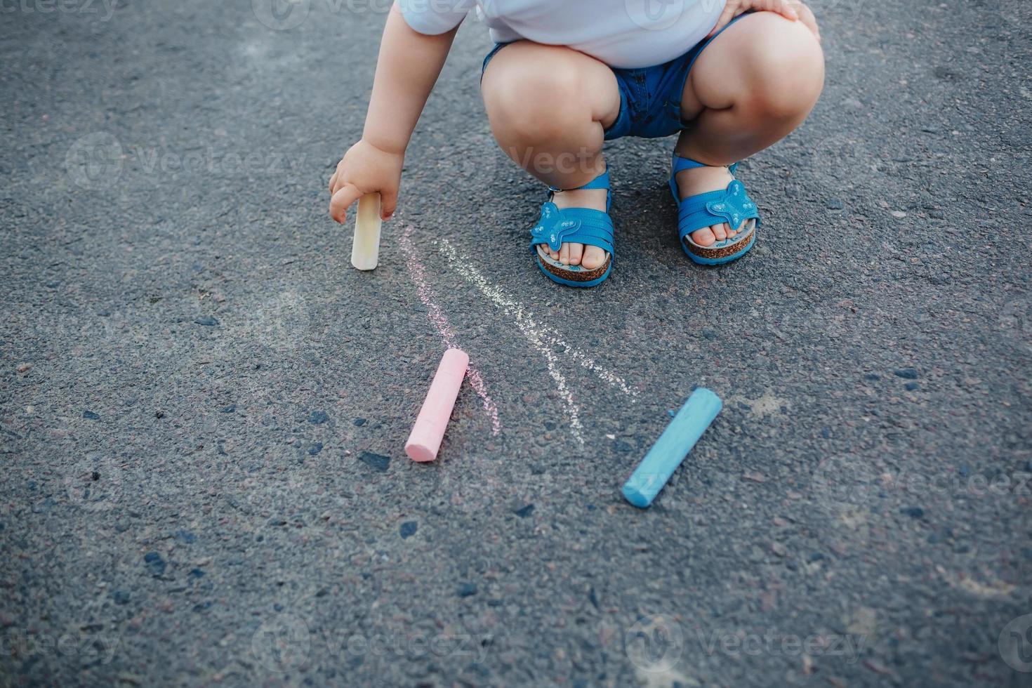 närbild av liten flicka ritar med kritor på trottoaren foto