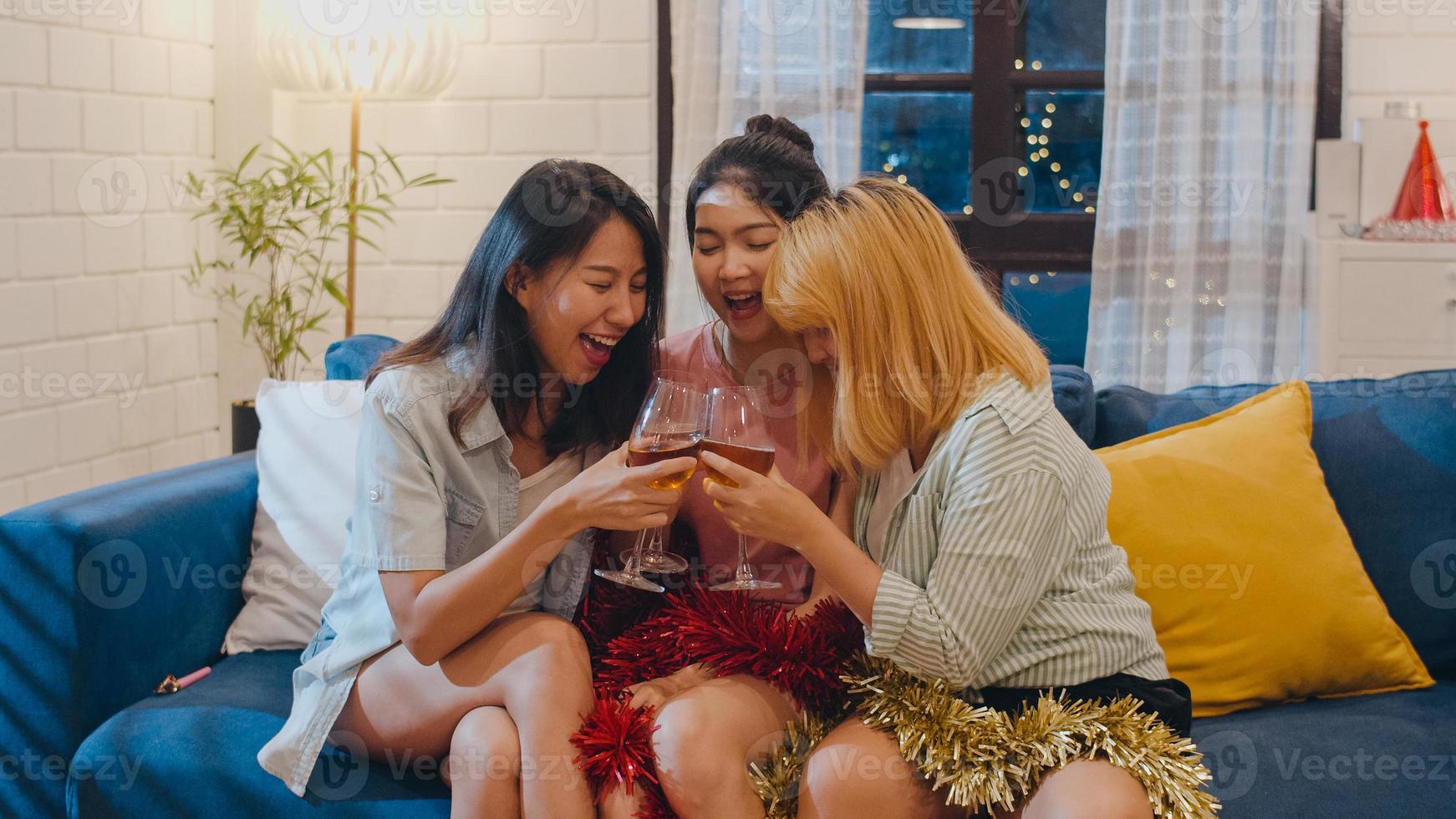 grupp av asiatiska kvinnor festar hemma, kvinnliga dricker cocktail pratar ha roligt tillsammans på soffan i vardagsrummet på natten. tonåring ung vän spela spel, vänskap, fira semester koncept. foto