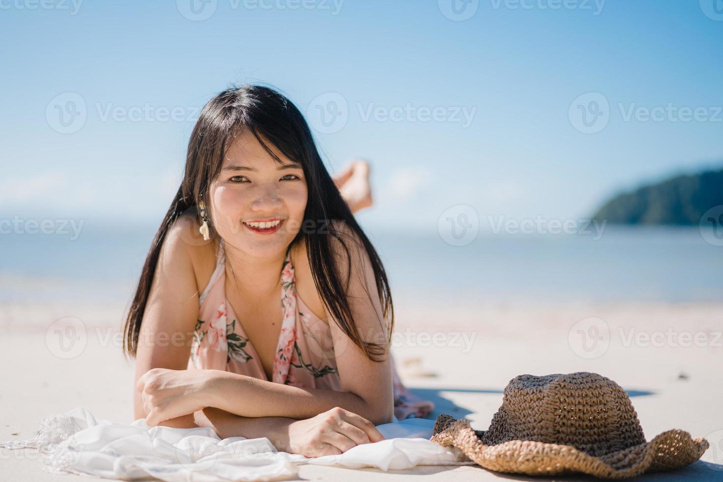 vacker ung asiatisk kvinna liggande på stranden glad koppla av nära havet. livsstil kvinnor reser på stranden koncept. foto