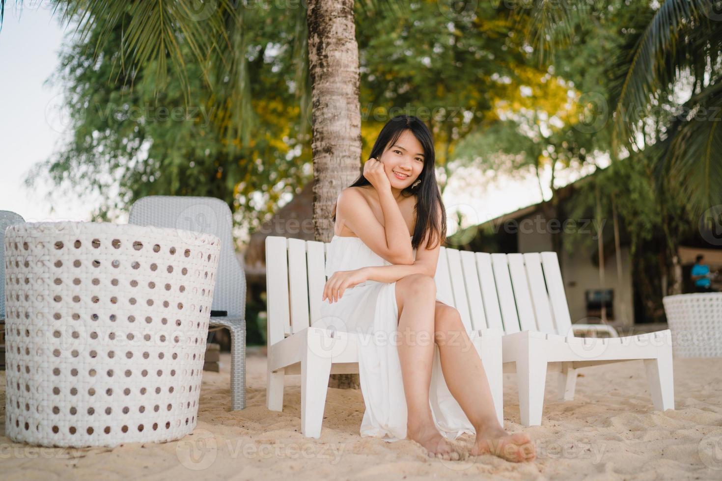 ung asiatisk kvinna sitter på bänken slappna av på stranden, vacker kvinna glad slappna av nära havet. livsstil kvinnor reser på stranden koncept. foto