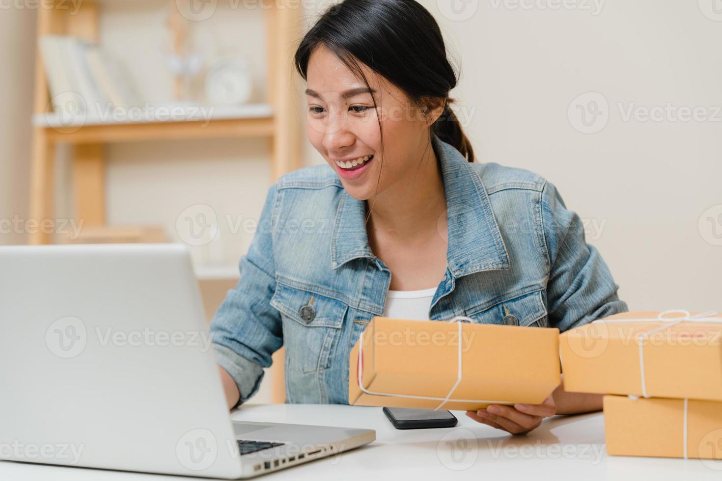 vacker smart asiatisk ung entreprenör affärskvinna ägare av sme online kontrollera produkt på lager och spara till dator som arbetar hemma. småföretagare hemmakontor koncept. foto