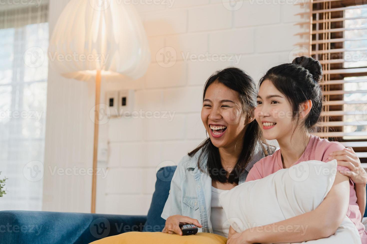 unga asien lesbisk hbtq kvinnor par tittar på tv hemma, asiatisk älskare kvinnlig känsla glad roligt skratta tittar TV-serie film tillsammans medan liggande soffa i vardagsrummet hemma koncept. foto