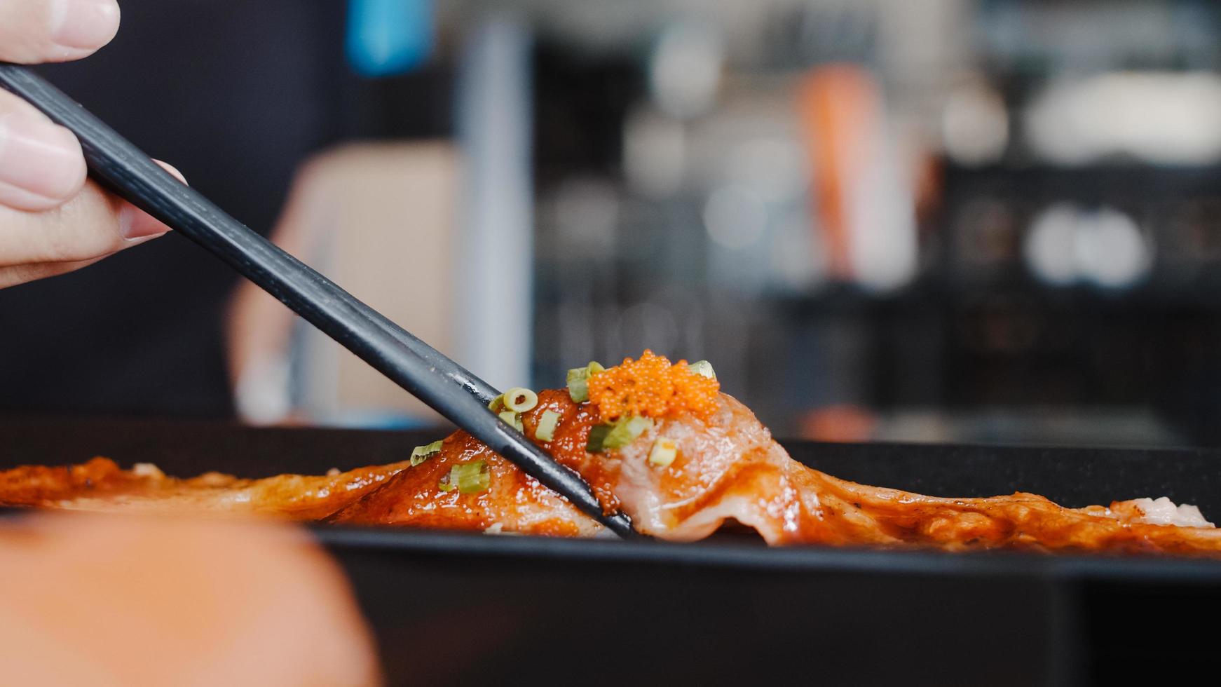 asiatisk kvinna som äter sushi på japansk restaurang, ung kvinna som håller ätpinnar och äter wagyu-biffsushi vid lunchtid på sommaren. livsstil kvinnor äter traditionell mat koncept. foto