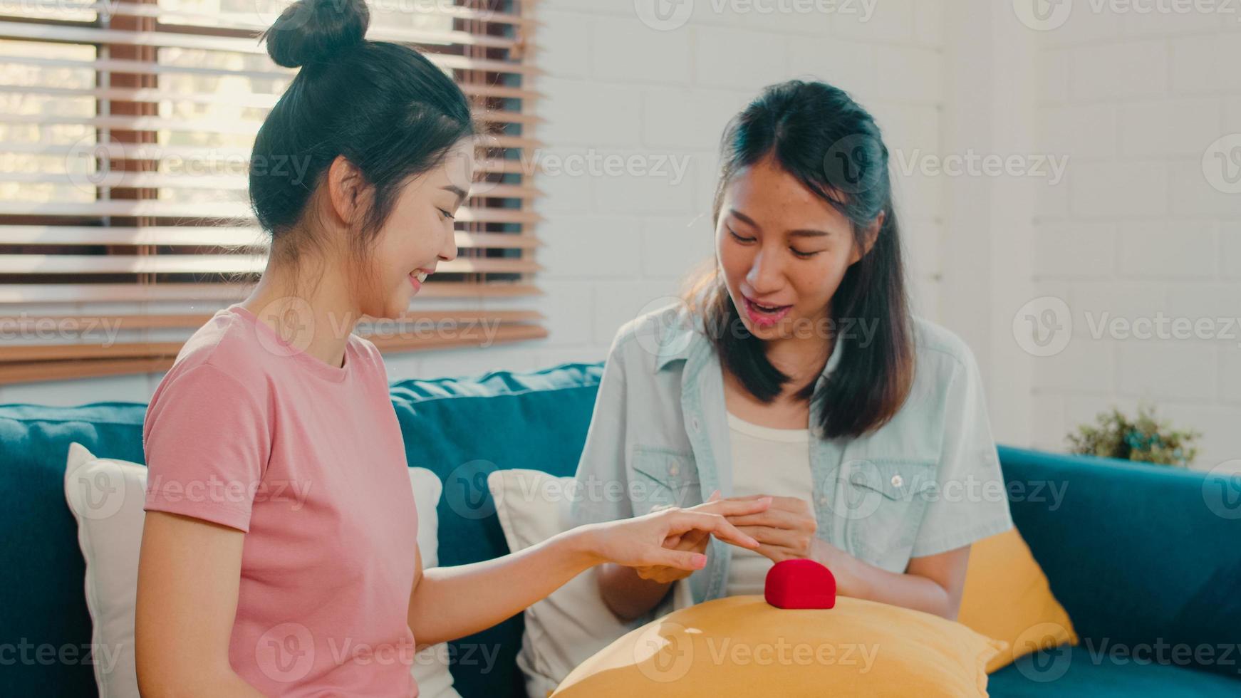 asiatisk lesbisk hbtq kvinnor par föreslår hemma, unga asien älskare kvinnliga glada leende har romantisk tid medan de föreslår och äktenskap överraskning bära vigselring i vardagsrummet hemma koncept. foto