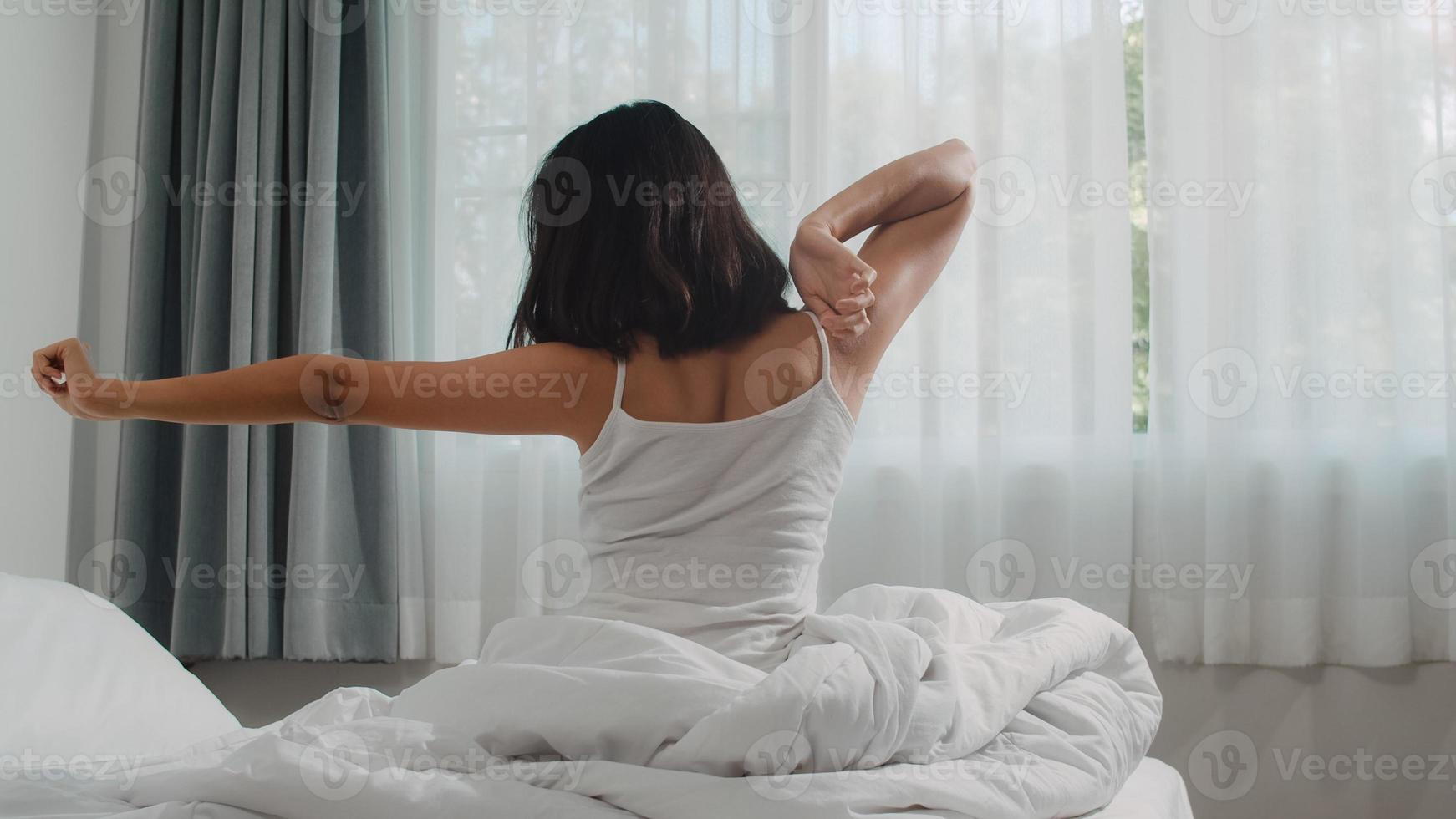 tonåring latinamerikansk kvinna vaknar hemma. ung asiatisk flicka stretching efter vaken sömn hela natten starta en ny dag med energi och vitalitet kände sig mycket utvilad på sängen nära fönstret i sovrummet på morgonen. foto