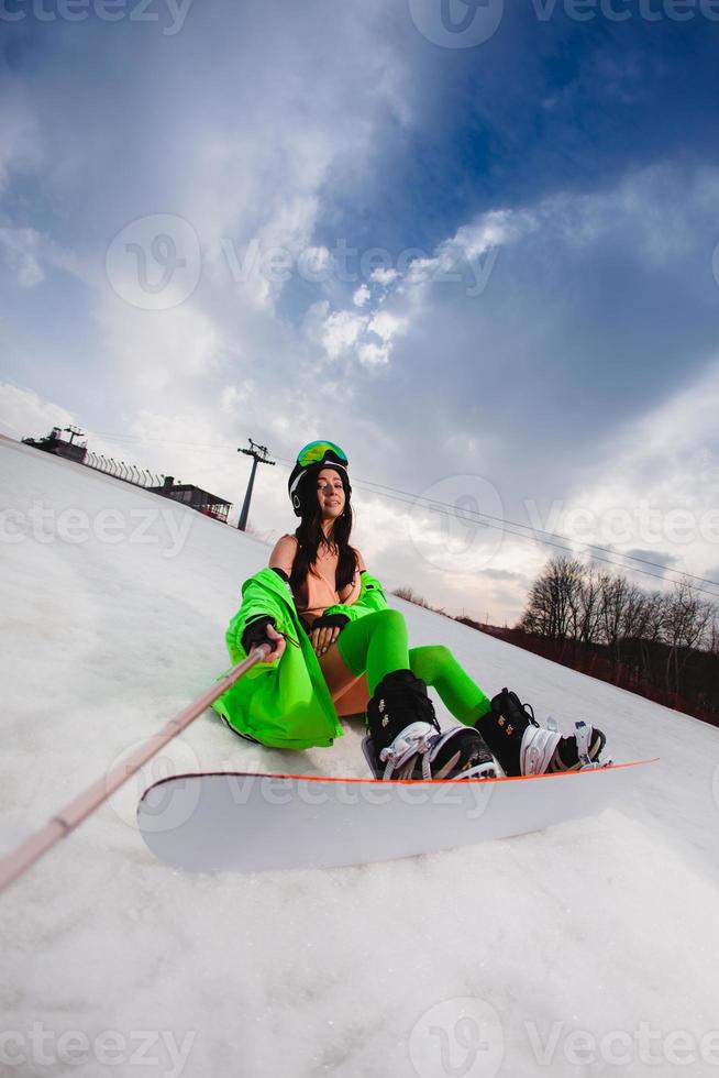 vacker kvinna som använder smartphone för att göra selfie med en snowboard i en skidbacke foto