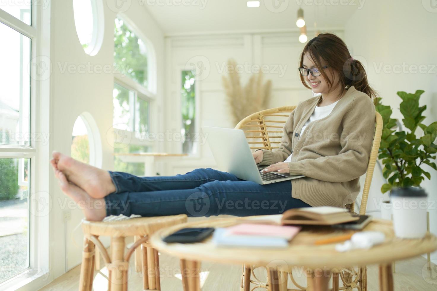 en ung kvinna sitter med benen sträckta med en bärbar dator i en bekväm hållning. foto