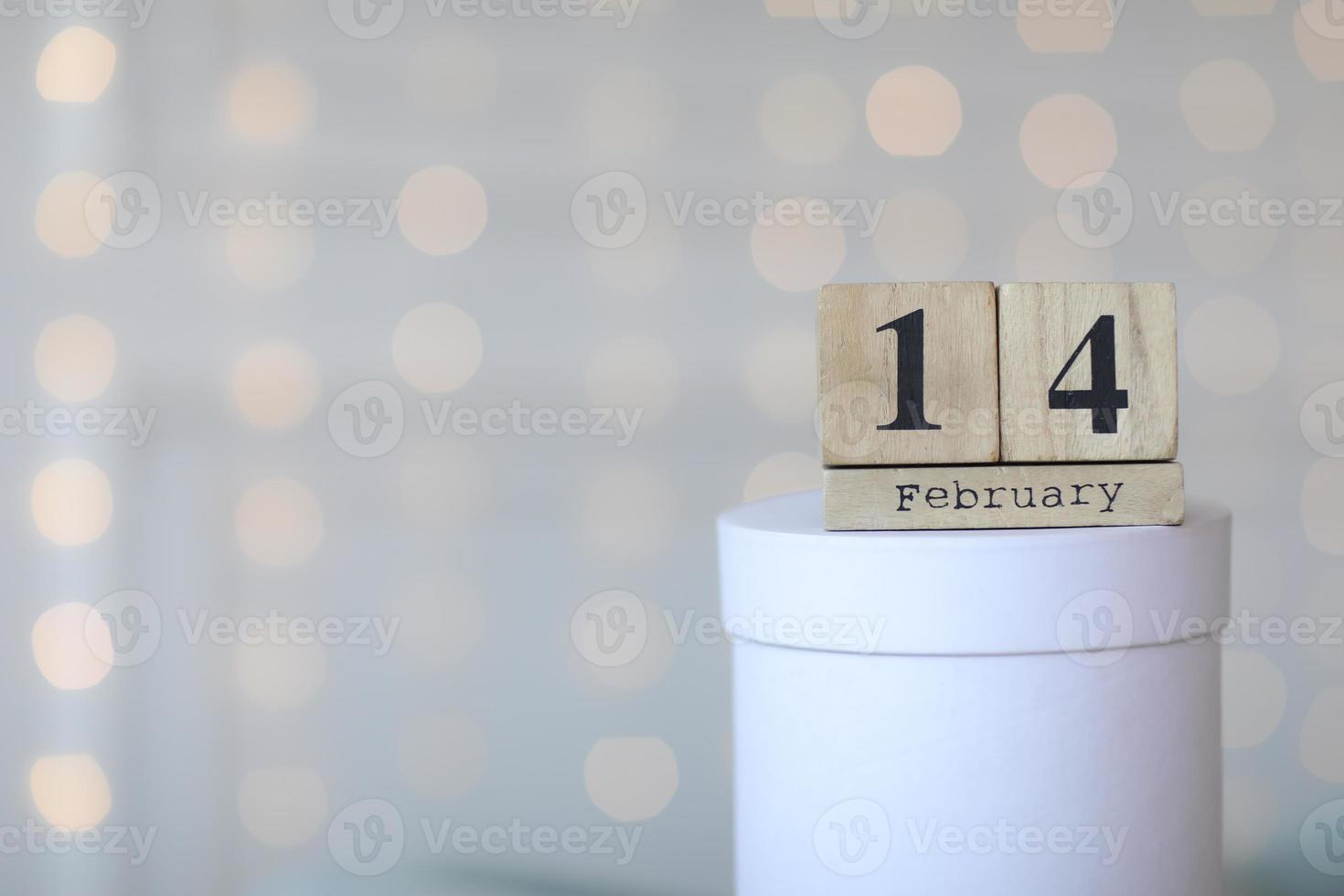 alla hjärtans dag koncept. datum 14 februari på träkubkalender på en vit presentförpackning och vitt hjärta i handen. bokeh gyllene och vit bakgrund foto