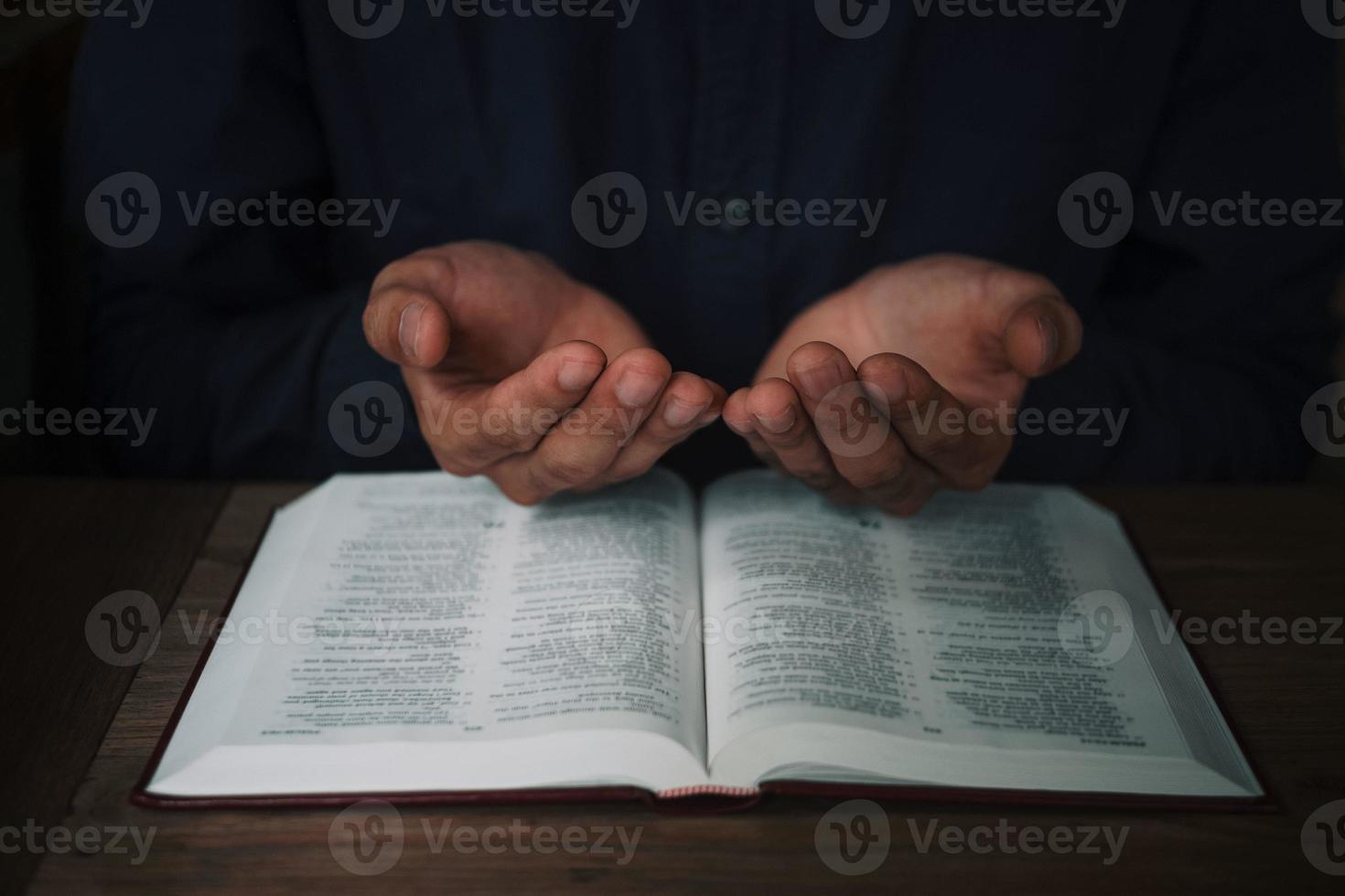 man läser och ber skriften eller bibeln på ett träbord med kopia utrymme. religion, tro koncept. foto