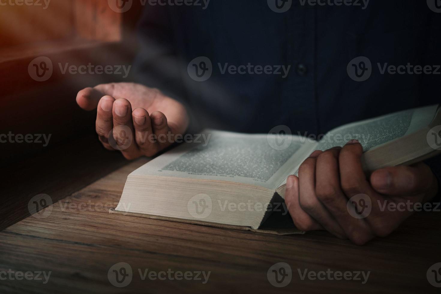 man läser och ber skriften eller bibeln på ett träbord med kopia utrymme. religion, tro koncept. foto