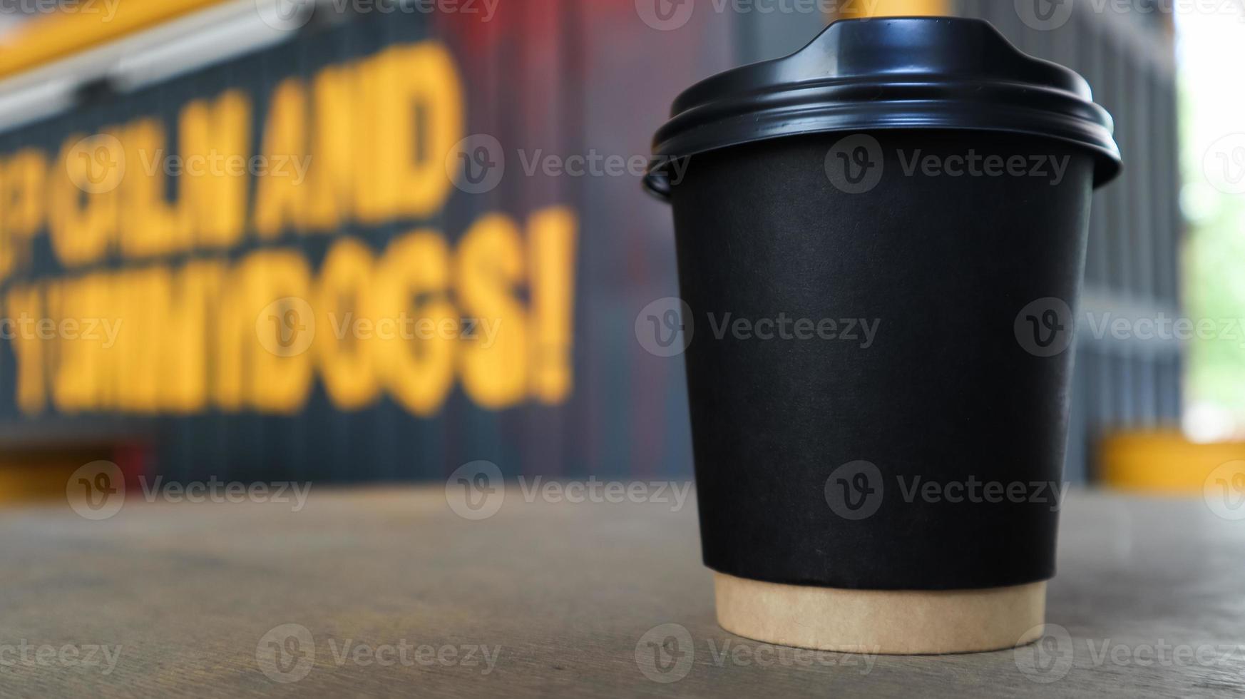 svart pappersmugg utan text och logotyp med kaffe med plastlock på ett träbord på ett gatukaffe i staden. kopieringsutrymme. foto