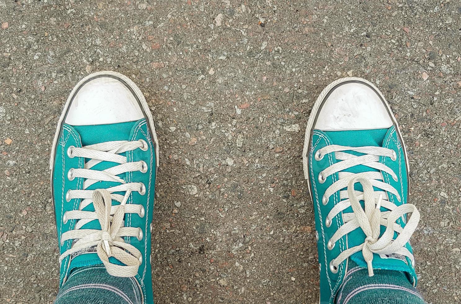 sneakers på asfaltvägen. utrymme för redaktionellt bruk. ovanifrån av gamla sneakerskor på en grå trottoarasfaltbakgrund. man står på grunge asfalt stadsgata, perspektiv perspektiv foto