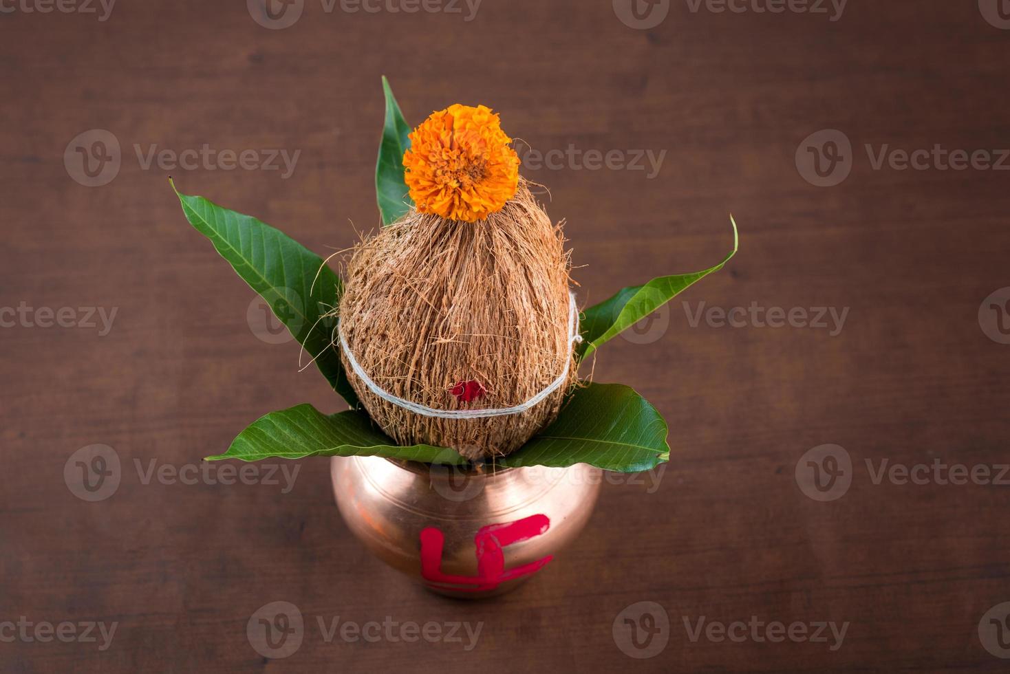 koppar kalash med kokos och mango blad med blomdekor på en trä bakgrund. väsentligt i hinduisk puja. foto