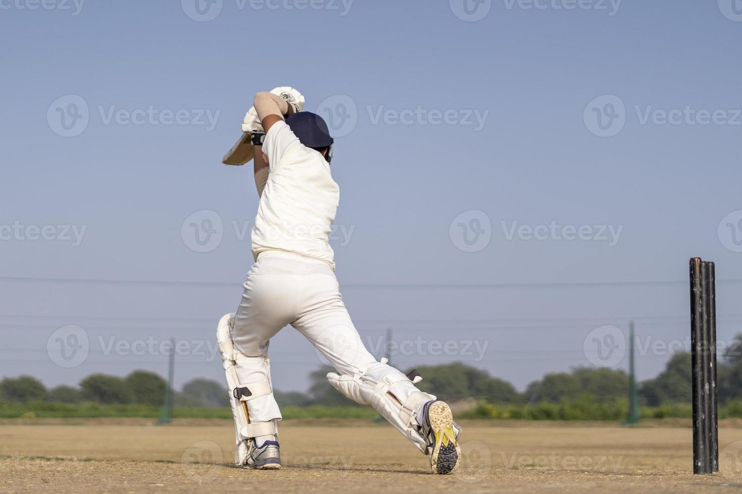 en cricketspelare som spelar cricket på planen i vit klänning för testmatcher. idrottsman som slår ett skott på cricketbollen. foto