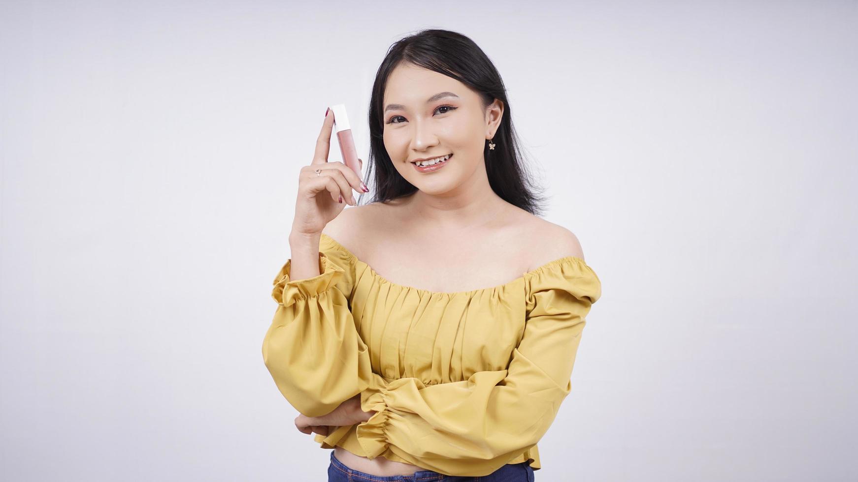 asiatisk flicka med smink visar läppstift i handen isolerad på vit bakgrund foto