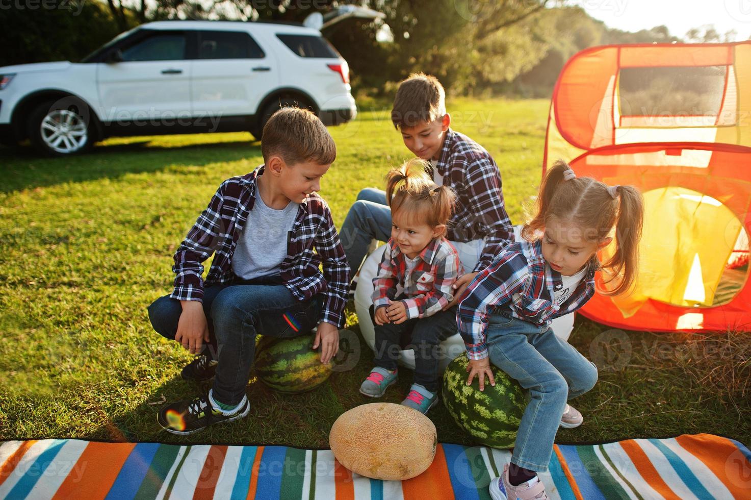 fyra barn tillbringar tid tillsammans. utomhus picknickfilt, sittande med vattenmeloner. foto