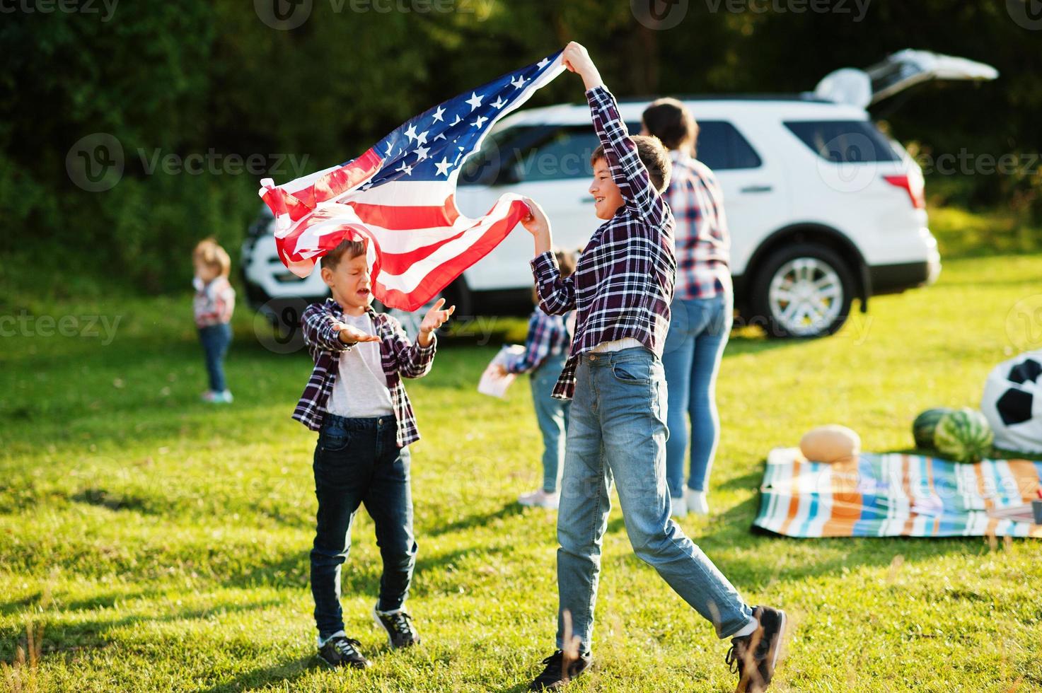 amerikansk familj tillbringar tid tillsammans. bröder leker med usa flaggor mot stor suv bil utomhus. amerika firar. foto